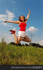 Woman in red t-shirt jumping high on a summer meadow under a blue sky, in the background a power pole is to be seen