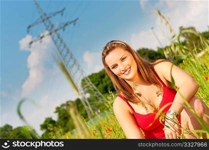 Woman in red t-shirt standing in meadow or grain field under a blue sky, in the background a power pole is to be seen