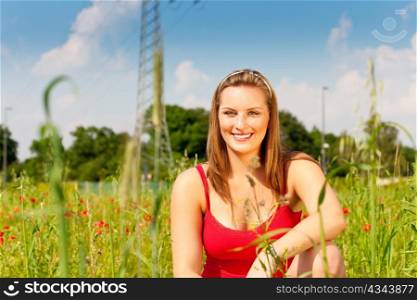 Woman in red t-shirt standing in meadow or grain field under a blue sky, in the background a power pole is to be seen