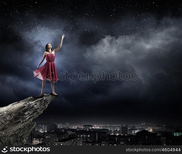 Woman in red. Young attractive woman in red dress standing on rock edge