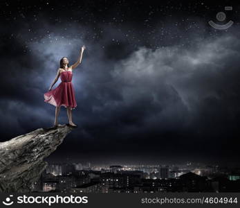 Woman in red. Young attractive woman in red dress standing on rock edge