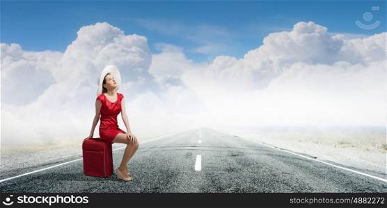 Woman in red. Young woman in red dress on road sitting on her red luggage