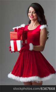 Woman in santa dress with gift. Beautiful young woman in Santa dress celebrating Christmas holding gift boxes