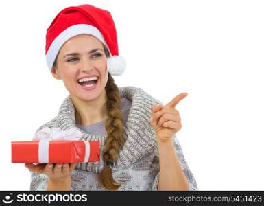 Woman in Santa hat holding Christmas gift and pointing on copy space