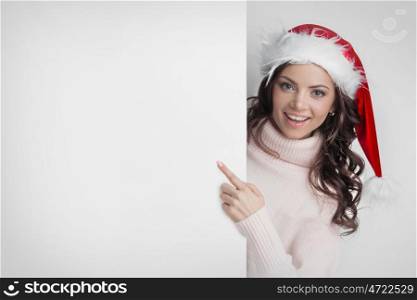 Woman in Santa's hat pointing at white copyspace