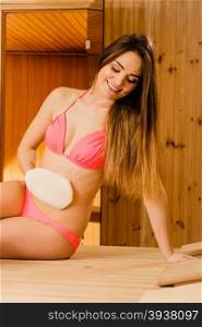 Woman in sauna with exfoliating glove. Skincare.. Young woman in wood finnish spa sauna massaging skin with exfoliating glove. Girl in bikini relaxing. Skincare concept.