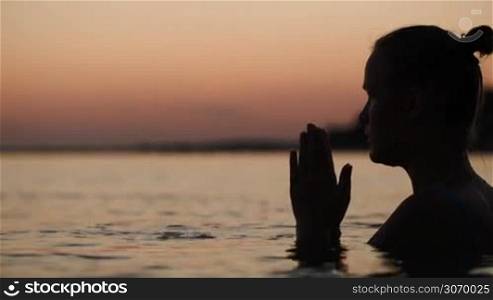 Woman in sea at sunset praying or meditating