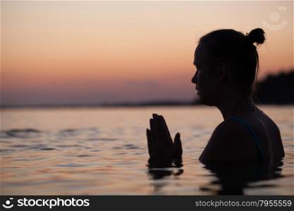 Woman in sea water at sunset alone. She praying or meditating