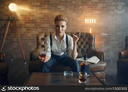 Woman in shirt and trousers sitting at the table with whiskey, retro fashion, gangster style. Vintage business lady. Woman at the table with whiskey, gangster style