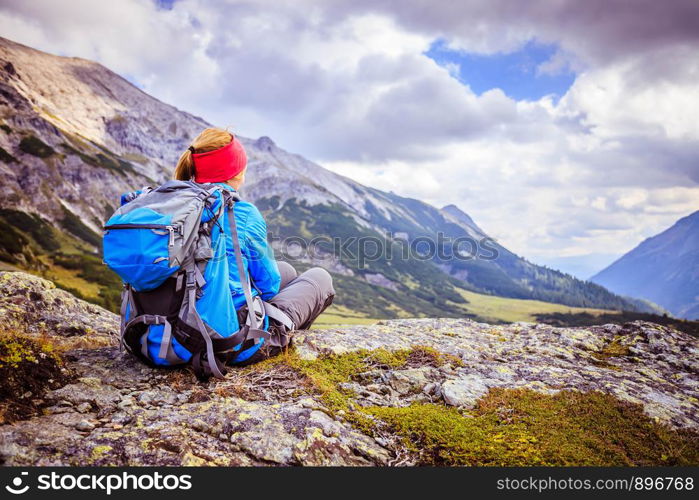 Woman in sportswear and with backpack is sitting on the stony ground and enjoys the view, in the mountains