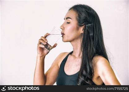 Woman in sportswear drinking water in a fitness gym. Healthy lifestyle and hydration concept.