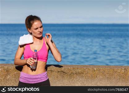 Woman in sportswear takes a break to rehydrate drinking water from plastic bottle, resting after sport workout outdoor by seaside. Woman drinking water after sport gym outdoor
