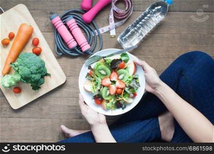 Woman in sportwear holding a dish of fresh salad with strawberries and kiwi, Healthy lifestyle