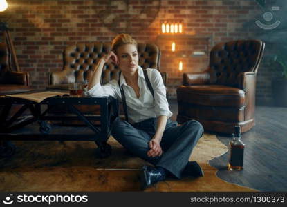 Woman in strict clothes relax on the floor with whiskey and cigar, retro fashion, gangster style. Vintage business lady in office with brick walls. Woman relax with whiskey and cigar, retro fashion