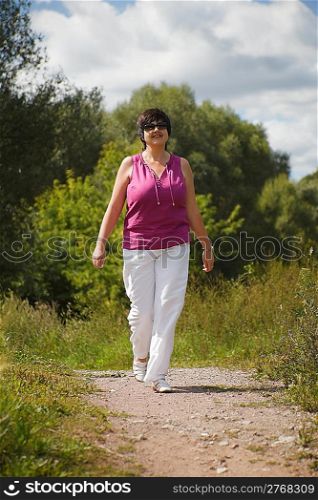 woman in sunny day on wood clearing goes at pathway, in sunglasses
