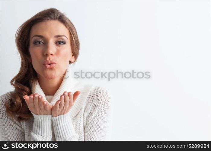 Woman in sweater blowing kiss. Studio portrait of beautiful long-haired woman in hot sweater blowing a kiss on white background