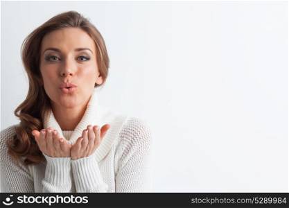 Woman in sweater blowing kiss. Studio portrait of beautiful long-haired woman in hot sweater blowing a kiss on white background