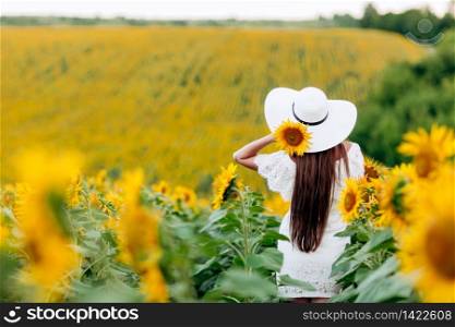 Woman in the field of sunflowers. A happy, beautiful young girl in a white hat is standing in a large field of sunflowers. Summer time. Back view. selective focus. Woman in the field of sunflowers. A happy, beautiful young girl in a white hat is standing in a large field of sunflowers. Summer time. Back view. selective focus.