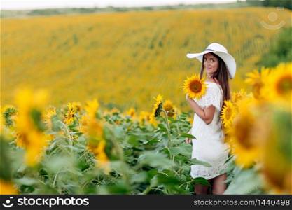 Woman in the field of sunflowers. A happy, beautiful young girl in a white hat is standing in a large field of sunflowers. Summer time. Back view. selective focus. Woman in the field of sunflowers. A happy, beautiful young girl in a white hat is standing in a large field of sunflowers. Summer time. Back view. selective focus.