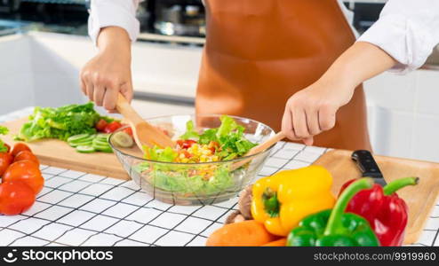 woman in the process of preparing healthy food Vegetable Salad mixing salad wooden spoon in kitchen at home Dieting Concept.