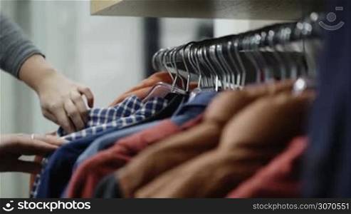 Woman in the shop looks through the male jackets and shirts, which are hanging on the racks