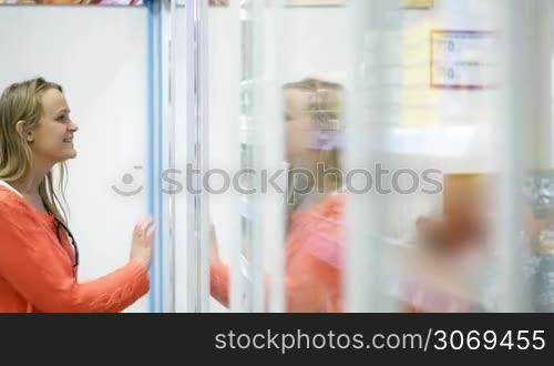 Woman in the shop opening pocket door of the showcase and taking a tube with cosmetic