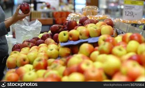 Woman in the supermarket coming up to the fruit counter. She choosing and putting apples in plastic bag