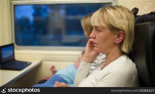 Woman in the train talking on the phone. Mother with son watching movie in background