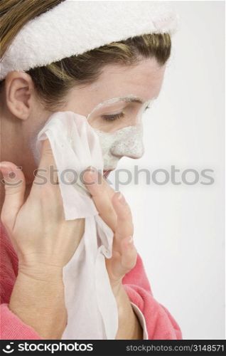 Woman in thirties wiping facial mask from her face. Wearing bath robe. Shot in studio.