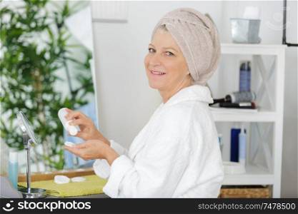 woman in towel applying cream and doing massage for face