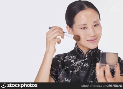 Woman in traditional clothing looking into a mirror and applying make up with a make up brush, studio shot