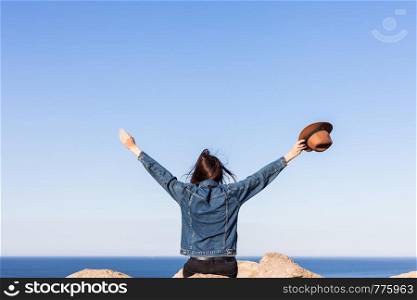Woman in travel clothes and hat sitting and looking at blue ocean and sky. Travel concept photo. Woman in travel clothes and hat sitting and looking at blue ocean and sky.