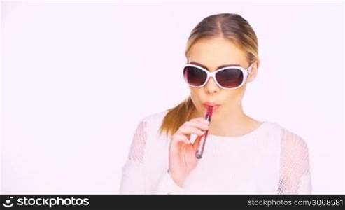 Woman in trendy stylish glasses smoking an e-cigarette puffing out a cloud of smoke at the camera isolated on white