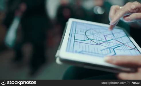 Woman in underground examines the metro map using the tablet, people passing by. Then she stands up and goes away