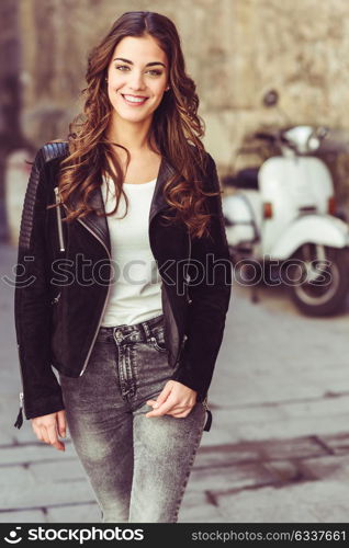 Woman in urban background smiling and wearing casual clothes with a old scooter in the background