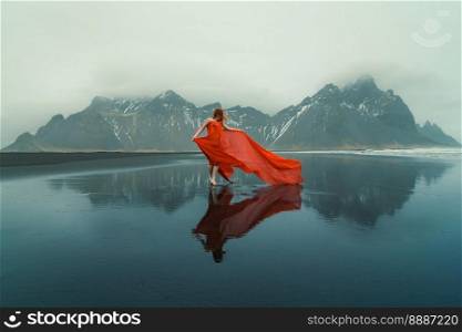 Woman in waved red dress on Reynisfjara beach scenic photography. Picture of person with mountains on background. High quality wallpaper. Photo concept for ads, travel blog, magazine, article. Woman in waved red dress on Reynisfjara beach scenic photography