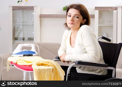 Woman in wheelchair ironing at home 