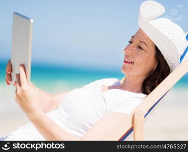 Woman in white clothes on the beach with tablet. Always connected