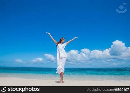 Woman in white dress posing in tropical sea beach with arms raised. Woman in dress on beach