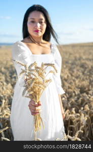 Woman in white dress stands in field with wheat. Person hold in hands bundle of ripe spikelets. Harvest season. High quality photo. Woman in white dress stands in field with wheat. Person hold in hands bundle of ripe spikelets. Harvest season.