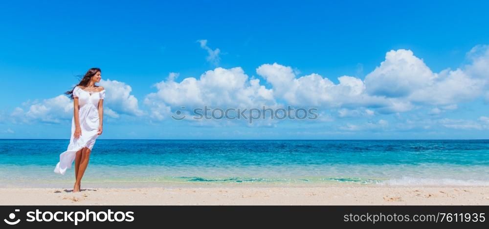 Woman in white dress walking on tropical beach, tropical sea on background. Woman in dress walking on beach