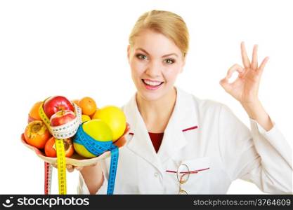 Woman in white lab coat holding fruits and colorful measure tapes isolated. Doctor dietitian recommending healthy food showing ok okay hand sign gesture. Diet.