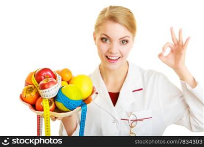 Woman in white lab coat holding fruits and colorful measure tapes isolated. Doctor dietitian recommending healthy food showing ok okay hand sign gesture. Diet.