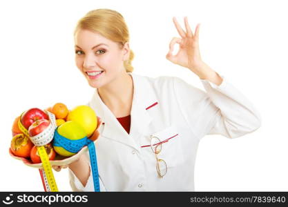 Woman in white lab coat holding fruits and colorful measure tapes isolated. Doctor dietitian recommending healthy food showing ok okay hand sign gesture. Diet.