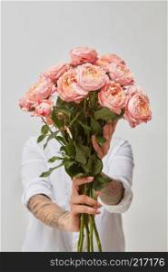 Woman in white shirt holding wedding bouquet of pink ranunculus on light background. Holidays and people concept. Girl holding flowers in her hands isolated on white background.