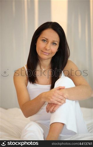 Woman in white sitting on a bed