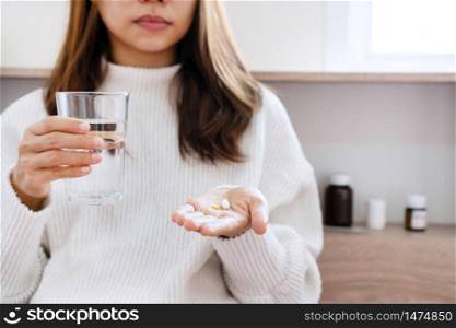 Woman in white sweater holding pill and glass of water in hands taking emergency medicine, supplements or antibiotic antidepressant painkiller medication to relieve pain, meds side effects concept, close up