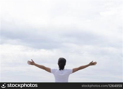 woman in white t-shirt raising her arms facing the sea