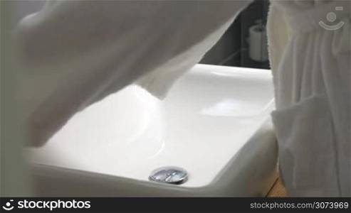 Woman in white terry robe in the bathroom. She taking liquid soap, washing hands and leaving