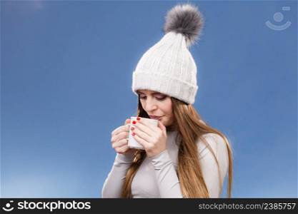 Woman in winter cap gray sports thermal underwear for skiing training holds mug with tea or coffee warming herself studio shot on blue. . girl in thermal underwear drinking tea